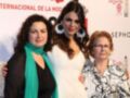 Tres mujeres posan juntas en un evento, con una de ellas luciendo un vestido blanco y joyas grandes. El fondo muestra un cartel con el nombre de Sevilla y la marca Sephora.