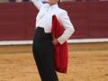 Un torero con chaqueta roja y traje blanco, en un ambiente de corrida.