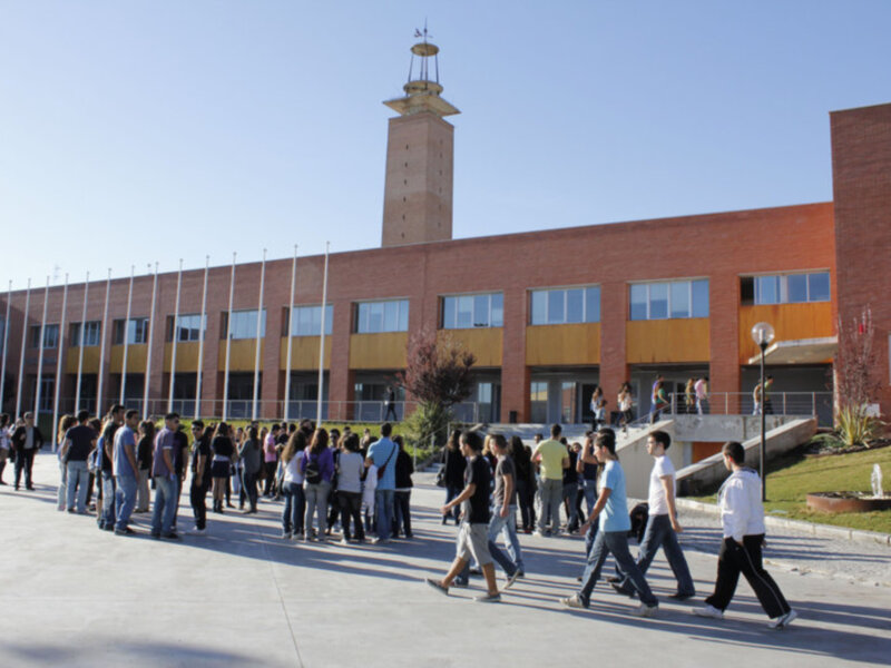 Un grupo de personas caminando en fila frente a un edificio con una torre en el centro.