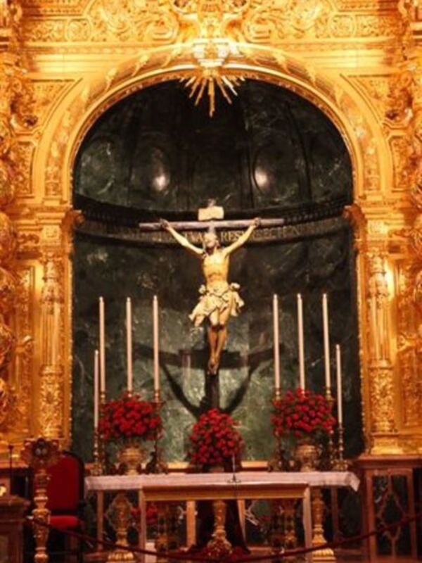 Cristo crucificado en una iglesia con dorados detalles y flores rojas.