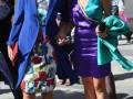 Dos mujeres en trajes de colores brillantes y accesorios florales posan para la foto. La imagen parece ser de una celebración o evento formal en un entorno urbano.