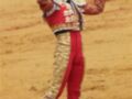 Un torero en traje tradicional, con guantes y un sombrero, celebrando una victoria en la plaza de toros.