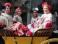 Las mujeres vestidas con trajes tradicionales españoles se sientan en un carruaje amarillo, disfrutando de una celebración festiva.