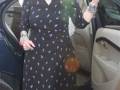 Una mujer con cabello blanco y rojo en la oreja, vestida con un vestido negro estampado de lunares multicolores y pantimedias negras, saliendo de un automóvil.