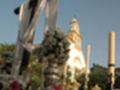 Una cruz de plata con flores y velas en un cementerio, con una iglesia en el fondo.