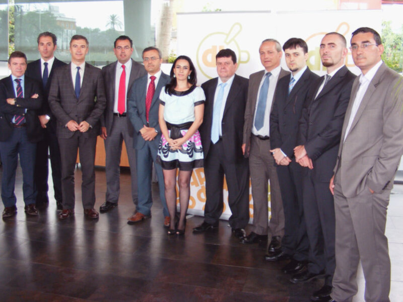 Equipo empresarial posando frente a un fondo con el logo de una empresa.