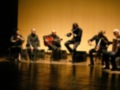 Orquesta de música clásica en escenario, con músicos tocando instrumentos tradicionales.