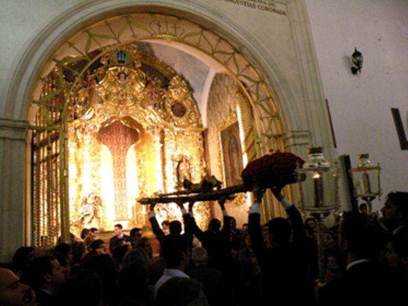 Una procesión religiosa en una iglesia con un altar dorado y una imagen central. La gente sostiene una estatua en el medio de la procesión.