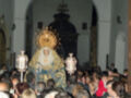 Una multitud congregada en una iglesia, con una imagen venerable de la Virgen en el centro. La arquitectura y vestimentas sugieren una celebración religiosa importante, posiblemente una procesión.