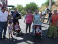 Familias participando en una procesión con carros de flores y caballos, en un entorno rural soleado.