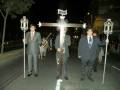 Procesión nocturna con cruces y faroles, con personas en trajes formales.