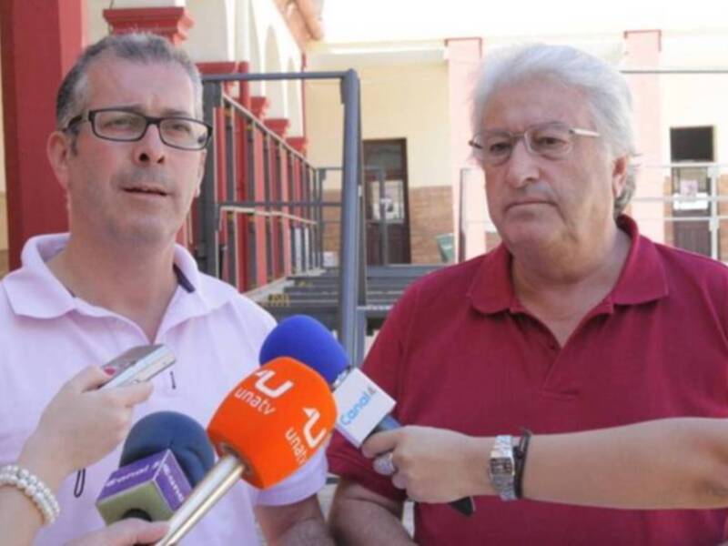 Dos personas son entrevistadas por un periodista con micrófonos de radio en una escena al aire libre, posiblemente en una institución pública.
