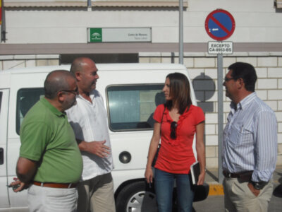 Cuatro personas charlan en un área de estacionamiento, frente a una furgoneta blanca y cerca de un cartel circular azul con la leyenda "EXCEPTO CA-953-85".