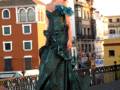 Elegante vestido verde con detalles azules en un desfile de moda en una ciudad histórica con edificios antiguos y arquitectura tradicional.