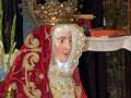 Figura religiosa con vestimentas rojas y doradas, coronada con una corona dorada, en un entorno de altar.