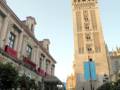 Una multitud de personas participa en una procesión religiosa frente a la Giralda, la famosa torre de Sevilla. La imagen captura el ambiente festivo y la arquitectura histórica del lugar.