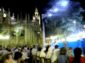 Fiesta nocturna en Sevilla con la Catedral iluminada y una multitud disfrutando de una actuación en escenario.