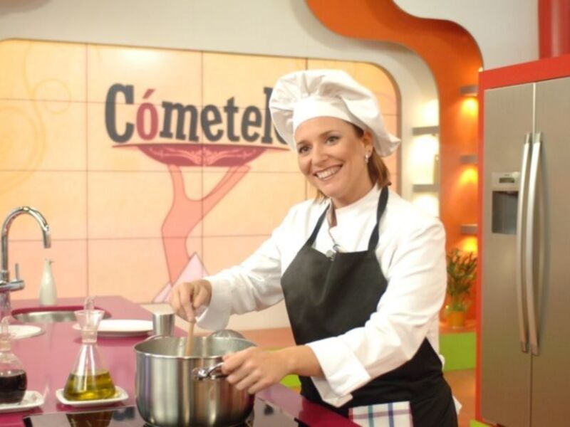 Una mujer en un programa de cocina, con una taza y un utensilio de cocina.