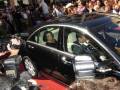 Una celebridad es conducida por un coche negro en el escenario de los premios Oscar, rodeada de fotógrafos y una multitud en el fondo.