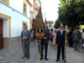 Hombres en trajes con palos y estandartes en una procesión en una calle urbana.