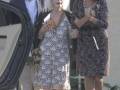 Una anciana con vestido floral y gafas de sol, caminando junto a una mujer joven en un entorno residencial.
