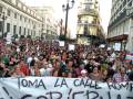 Una multitud se concentra en una calle, sosteniendo un cartel que dice "Toma la calle romper la corrupción". La imagen muestra una protesta pública en un entorno urbano con edificios históricos al fondo.