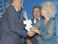 Una mujer sonríe mientras recibe un premio de manos de dos hombres. El fondo muestra una insignia con el nombre "VIII Premios Villa de Madrid".