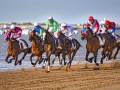 Competitivo galope de caballos en la playa con jinetes en carrera.