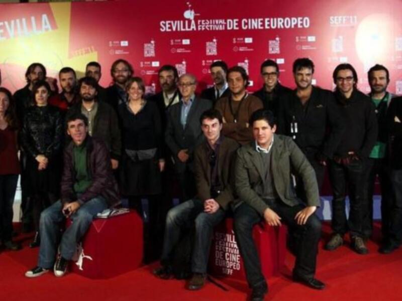 Grupo de personas posando en un escenario rojo con carteles del Festival de Cine Europeo de Sevilla.
