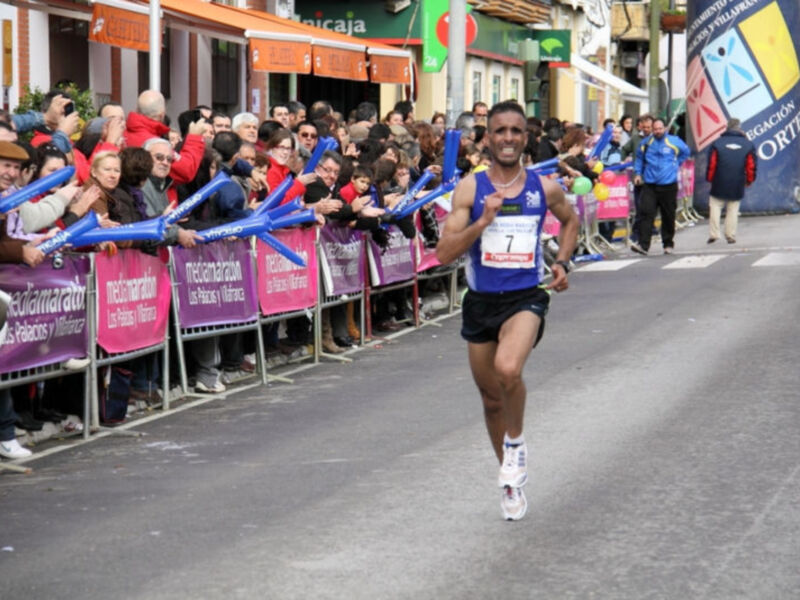 Atleta corriendo en una carrera de maratón, con público animando desde la orilla de la calle.