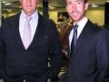 Dos hombres en trajes posan para la foto en un entorno formal.