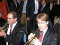 Dos músicos tocan trompetas en un ambiente formal, vestidos con trajes y corbatas.