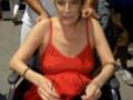 Una mujer en silla de ruedas con un vestido rojo, rodeada por personas y objetos.