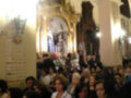 Interior de una iglesia con arcos y altares, lleno de personas asistiendo a una ceremonia o evento.