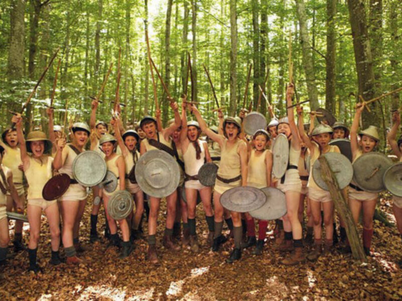 Una escena de una película o una representación teatral donde un grupo de personas vestidas de manera antigua, con cascos y armas, se encuentran en un bosque.