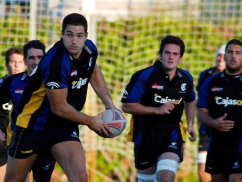 Jugadores de rugby en acción durante un partido, con un jugador en primer plano controlando el balón.