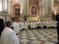 Imagen de un grupo de sacerdotes vestidos con hábitos blancos y rojos, posiblemente durante una ceremonia religiosa en un edificio histórico con arcos y vitrales.