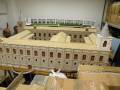 Un maqueta de un edificio histórico, posiblemente una catedral o palacio, con detalles arquitectónicos y un techo inclinado. La maqueta está colocada en una superficie con cajas de cartón alrededor.