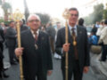 Dos hombres en trajes con medallas y bastones dorados, posando en una reunión pública al aire libre.