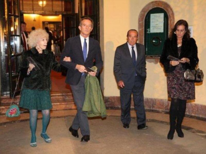 Personajes en trajes y vestidos caminando por un pasillo interior.