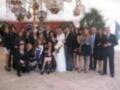 Una boda con una novia en blanco, un novio en negro y varias personas vestidas formalmente.