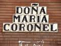 Un letrero de madera con la frase "DOÑA MARÍA CORONEL" en letras negras sobre un fondo de madera.