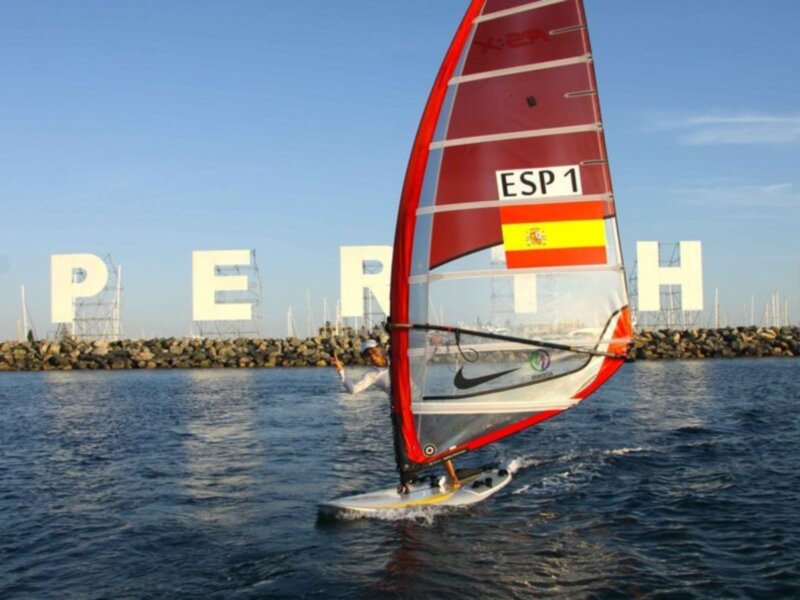 Un windsurfer con el número ESP 1 compite en aguas limpias frente a las letras gigantes de 'PER' en Perth, Australia.