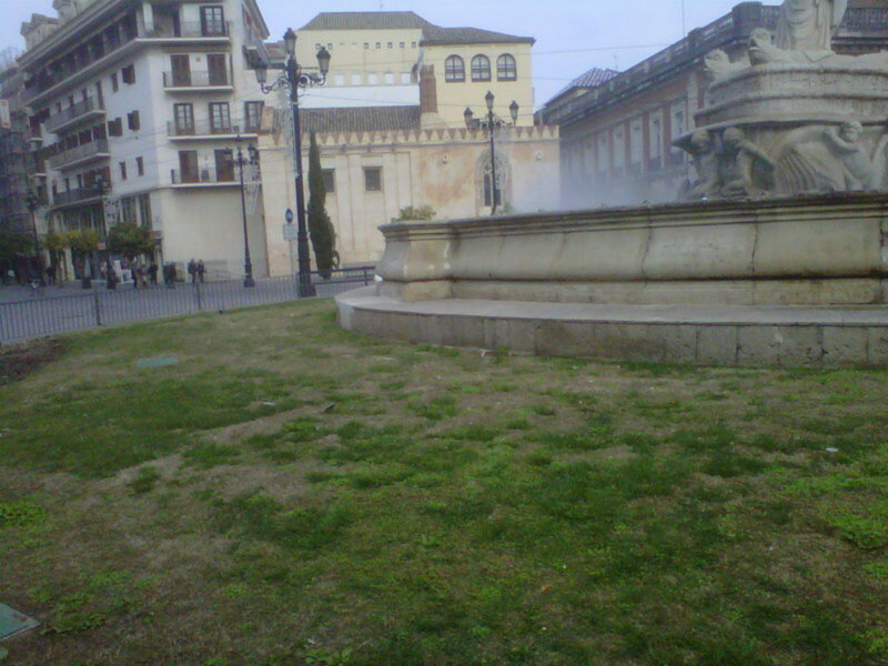 Un parque con una fuente antigua y un edificio histórico en el fondo.