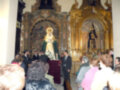 Una multitud de personas se reúne en un templo para rendir homenaje a una imagen religiosa, destacando el altar dorado y la presencia de dos estatuas en el fondo.