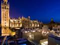 Catedral de Sevilla iluminada de noche con piscina en el techo y el Giralda en el horizonte.