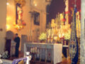 Interior de una iglesia durante un servicio religioso, destacando el altar adornado con velas y flores.