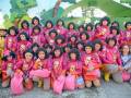 Grupo de niñas vestidas con trajes rosados y sombreros, posando con bolsas y medallas en un evento festivo.
