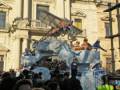Una caravana de carnaval con figuras de dragones y personajes en un escenario de carnaval, con un edificio histórico en el fondo.