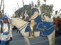 Imagen de un desfile navideño con personajes vestidos de época y montados en caballos.